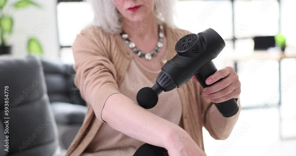 Elderly old woman relaxing hand massage in vibrating massager. Massage gun and pain relief concept Elderly old woman relaxing hand massage in vibrating massager. Massage gun and pain relief concept