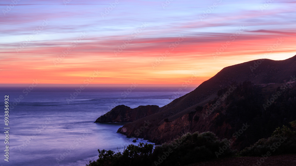 Mountain slopes into Pacific Ocean on rugged coast with beautiful sunset
