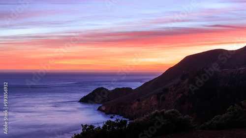 Mountain slopes into Pacific Ocean on rugged coast with beautiful sunset