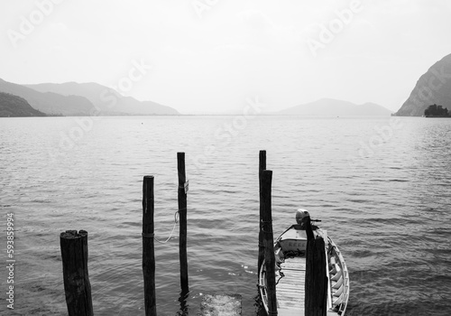 Old wooden pier with a boat on the coastline of Monte Isola (Mount Island), an island in the middle of Lake Iseo, Italy. Italian alps on the horizon, monochromatic. photo