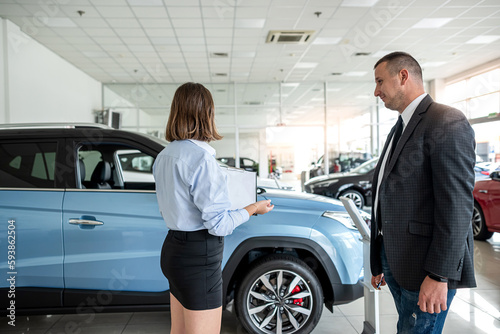 Female dealer in suit holding clipboard help with purchase new car her client © RomanR
