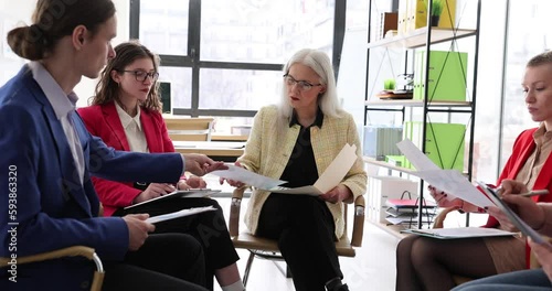 Serious mature woman team leader coach teaches team to explain business plan in group meeting. Collaboration project and business development discussion