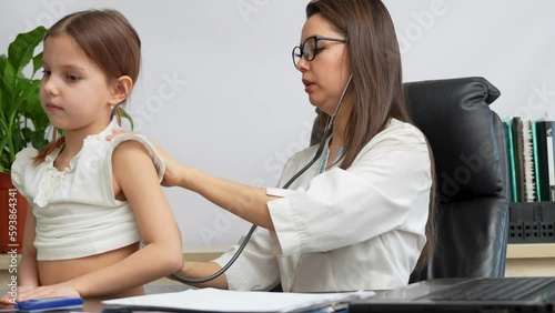 Female doctor pediatrician using stethoscope listen heart of cute girl photo