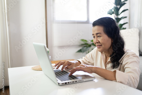 Middle age Asian woman Work from home. senior woman smiling Beautiful mature asian woman on laptop with technology concept © Charlie's