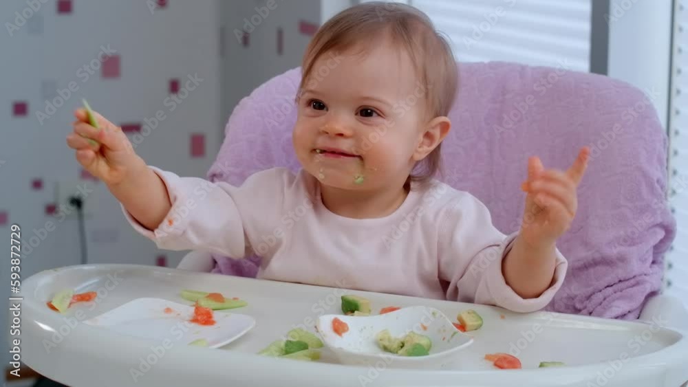 Toddler baby girl eating lunch by herself and throwing food on the floor in the kitchen, baby lead weaning. Toddler baby girl eating lunch by herself and throwing food on the floor in the kitchen, baby lead weaning.