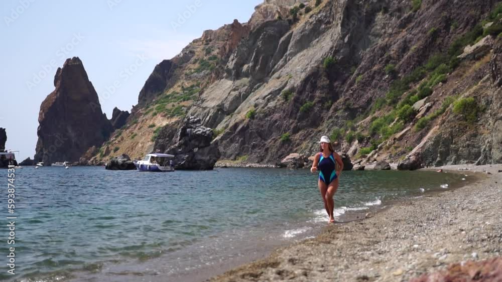 Well looking middle aged sporty woman with long hair, fitness instructor in blue swimwear enjoys the scenery in the mountains near sea. Female fitness trekking concept. Well looking middle aged sporty woman with long hair, fitness instructor in blue swimwear enjoys the scenery in the mountains near sea. Female fitness trekking concept.