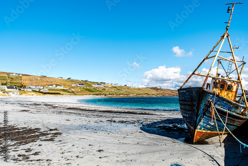 Abandoned boat or fishing trawler on Arranmore island  Republic of Ireland. The sun is shining on a rusty vessel stranded in Aphort Strand  County Donegal. Forsaken slanting ship on Irish white beach