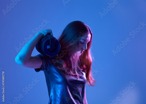 Stylish fashion teenager model  with headphones listening dj music dancing in purple neon lights. Young teen girl enjoy cool music 90s party mix in violet studio background