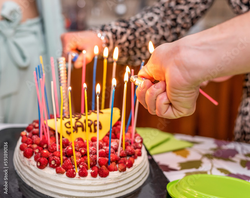 Happy birthday cake with colorful candles burning and many red wild strawberries
