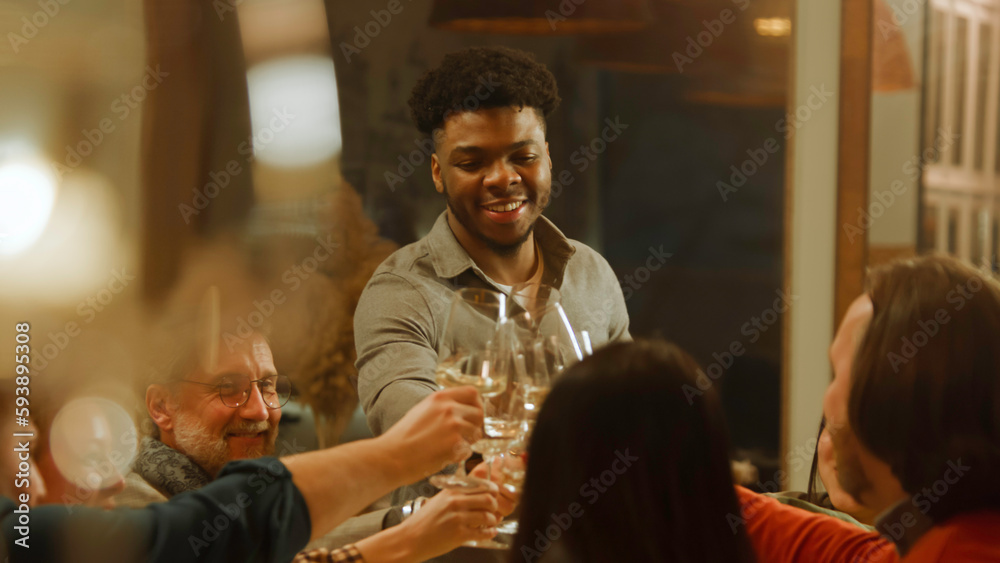 African American man says toast. Group of friends clink glasses and drink wine in restaurant. People spend evening together, hangout on birthday party in modern gastro cafe. Public catering concept.