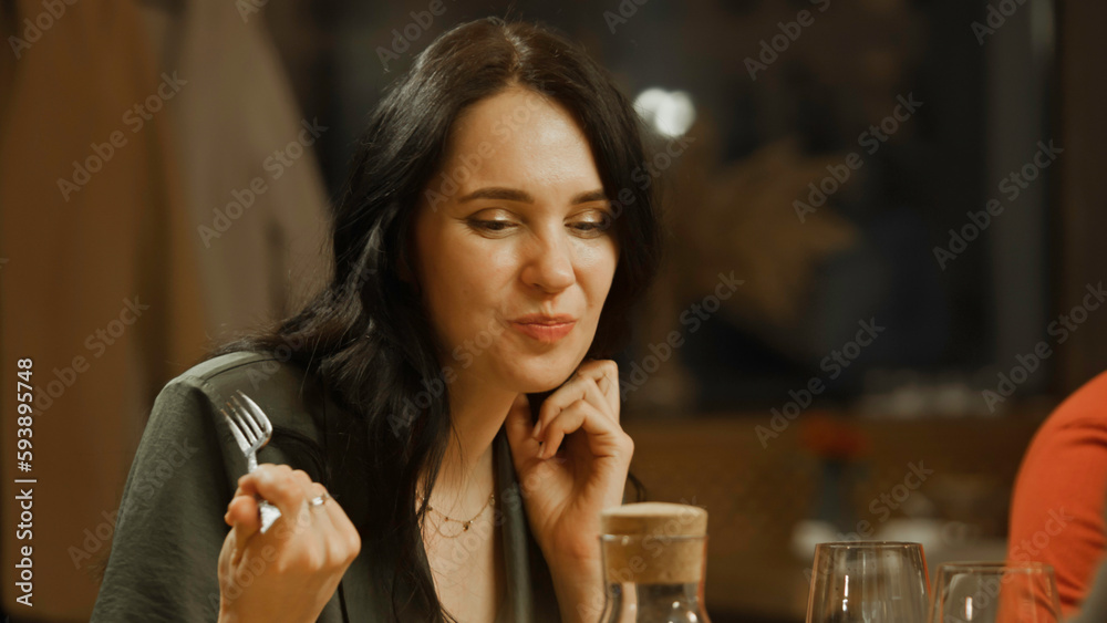 Close up shot of woman eating and enjoying delicious food, talking to friends in modern gastro cafe. She celebrates birthday, has family dinner, spends evening in restaurant. Concept of public eating. Close up shot of woman eating and enjoying delicious food, talking to friends in modern gastro cafe. She celebrates birthday, has family dinner, spends evening in restaurant. Concept of public eating.