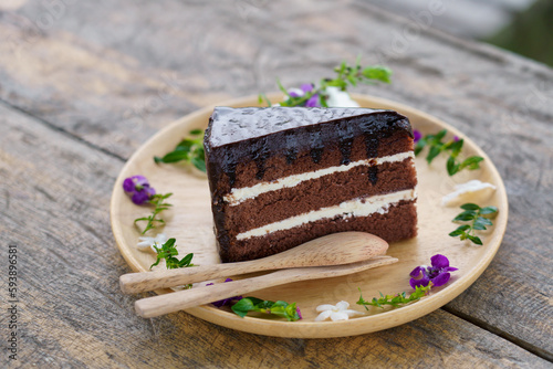 Chocolate cake. Slice of fudge chocolate with butter cream cake. Tasty homemade soft and delicious chiffon cake on table wooden plate with sweet purple flower on table. Bakery and dessert concept.