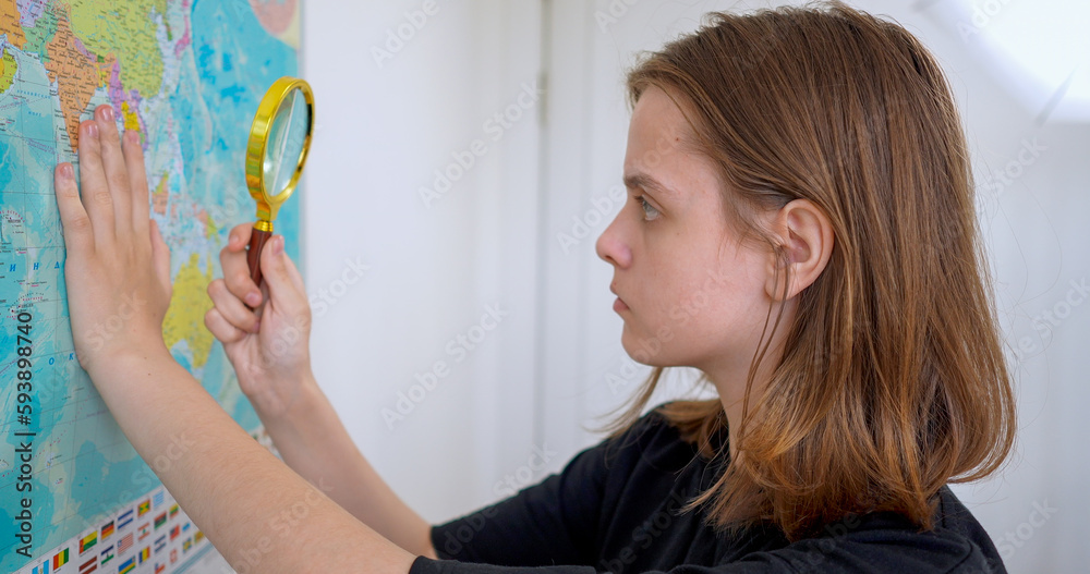 Fototapeta premium Teen girl seeking country on the map with magnifier