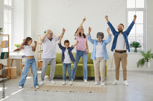 Happy extended multigenerational family all together having fun at home. Funny, overjoyed, excited mother, father, grandmother, grandfather and children dancing in a big, spacious living room interior