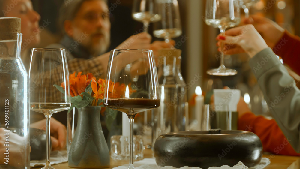 Close up shot of waiter pouring red wine from the bottle into the glass in restaurant. People clink glasses, celebrate birthday, spend weekend evening in modern gastro cafe. Public catering concept.