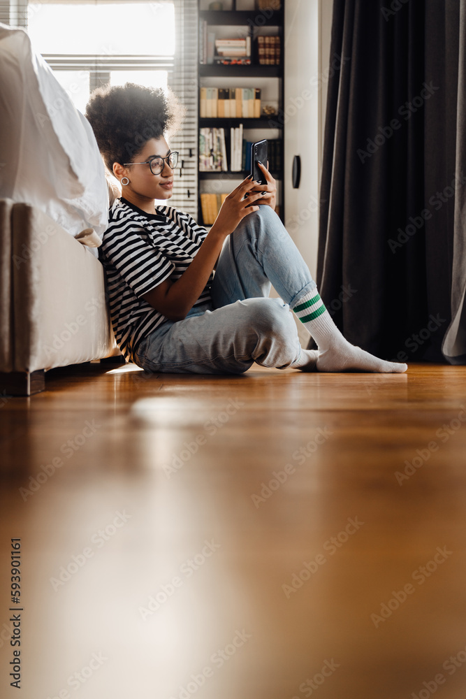 Beautiful african woman using mobile phone while sitting in bedroom Beautiful african woman using mobile phone while sitting in bedroom