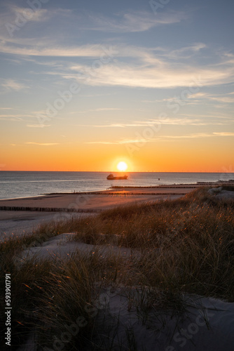Sunset photo on a dune with the beach and a ship on the North Sea coast in Zeeland, Netherlands
