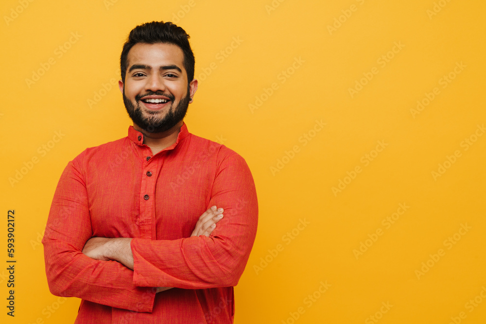 Young indian man smiling while standing with folded arms isolated over yellow background Young indian man smiling while standing with folded arms isolated over yellow background