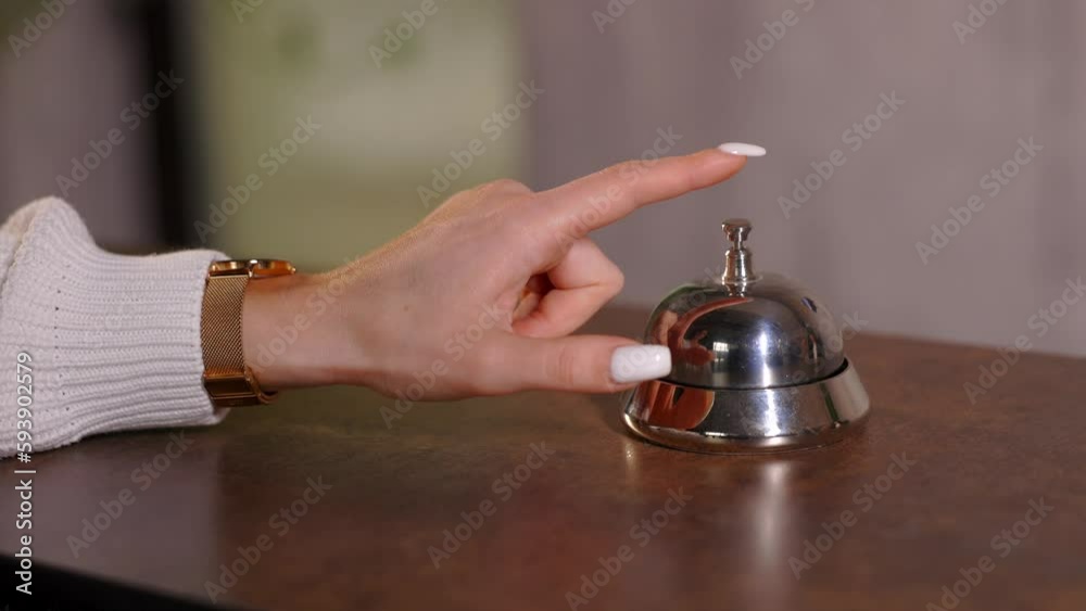 Hand of guest ringing bell on reception desk of in hotel.