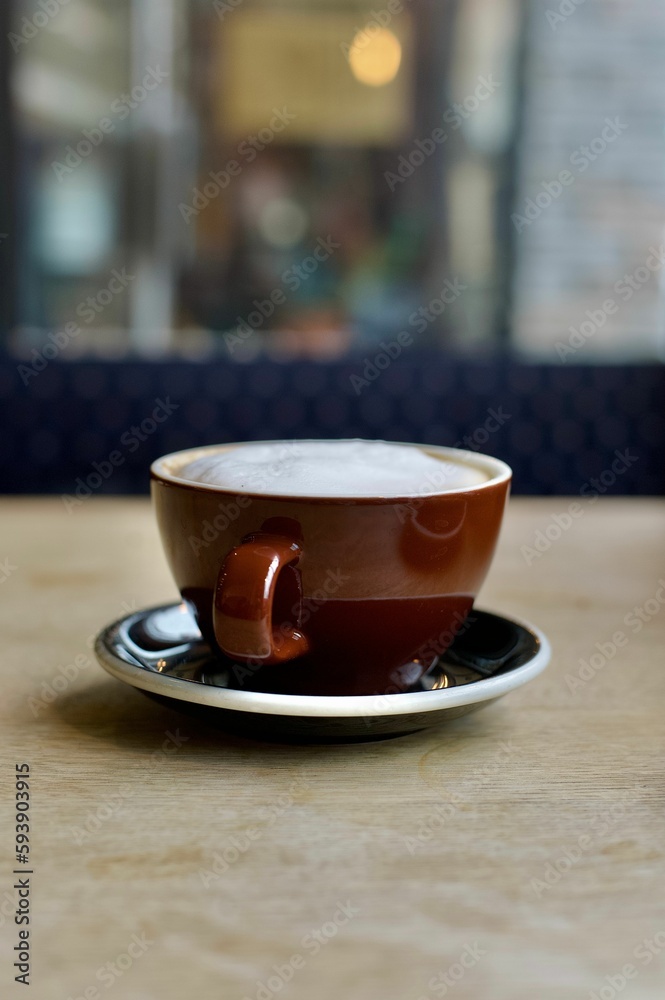 A cup of frothy cappuccino on a wooden table in a coffee shop