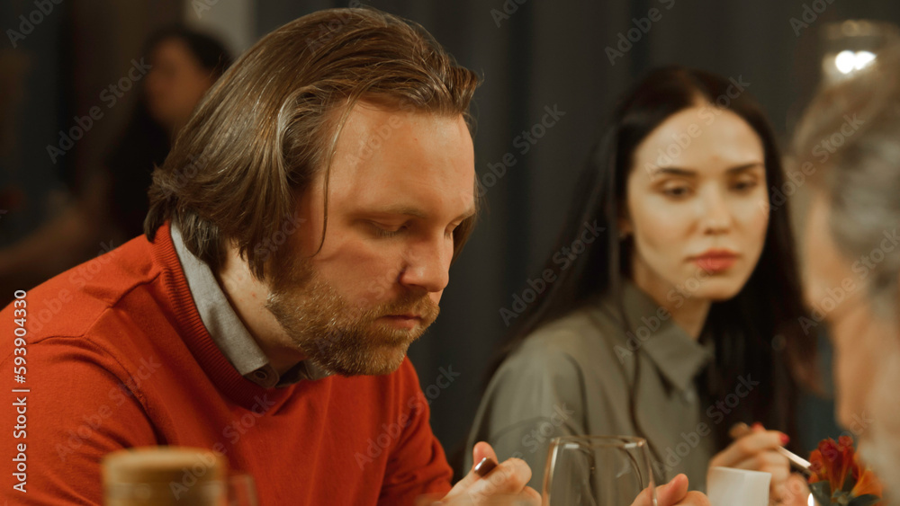 Close up shot of man eating delicious dish, smiling, talking with friends in modern gastro cafe. He has birthday party, family dinner, spends evening in restaurant. Concept of public eating. Zoom in. Close up shot of man eating delicious dish, smiling, talking with friends in modern gastro cafe. He has birthday party, family dinner, spends evening in restaurant. Concept of public eating. Zoom in.