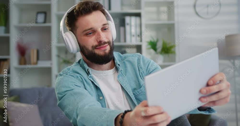 Man gamer holding digital tablet in headphones enjoying playing video games in light living room interior. Esport streaming game online. Gaming fun. Man gamer holding digital tablet in headphones enjoying playing video games in light living room interior. Esport streaming game online. Gaming fun.