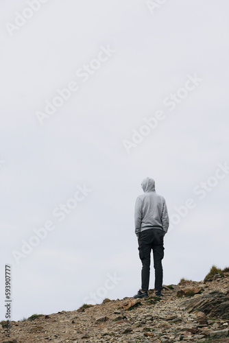 Man standing on the top of the mountain looking at the view. Tourist hiking in the mountains on a cloudy day. Lone man with space for text.