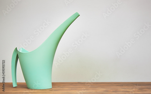 Green watering can for flowers on a wooden table close-up with blur.