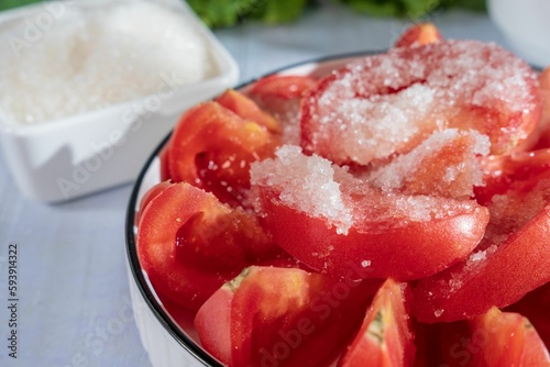 Closeup of delicious red tomato slices in a bowl with salt covering them on a breakfast table