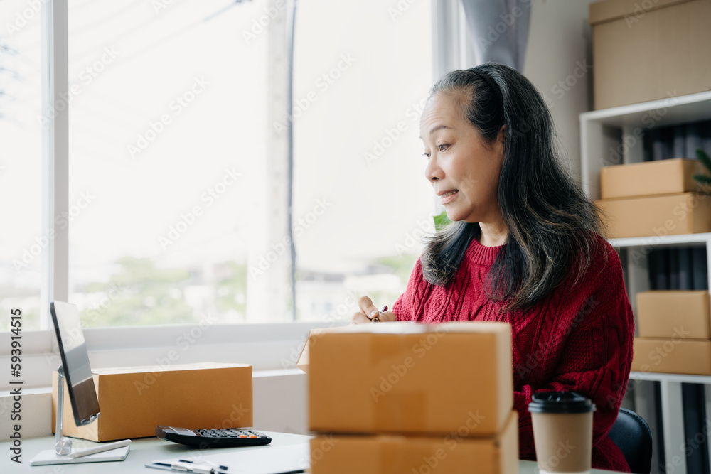 adult woman start up small business owner writing address on cardboard box at workplace.small business entrepreneur SME or freelance, female working with box at home. adult woman start up small business owner writing address on cardboard box at workplace.small business entrepreneur SME or freelance, female working with box at home.