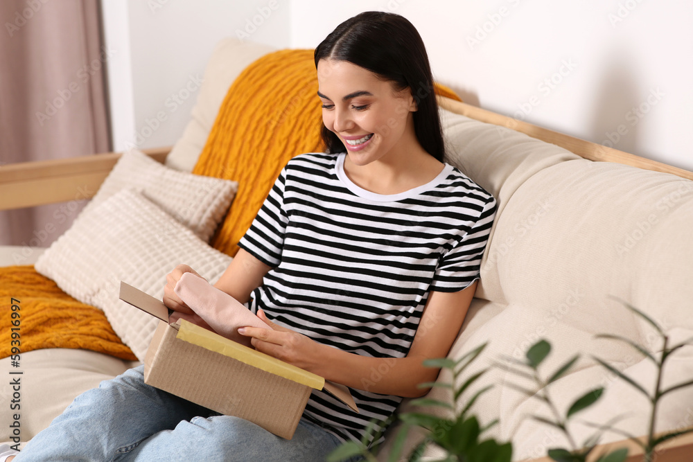 Happy young woman opening parcel on sofa at home. Internet shopping Happy young woman opening parcel on sofa at home. Internet shopping