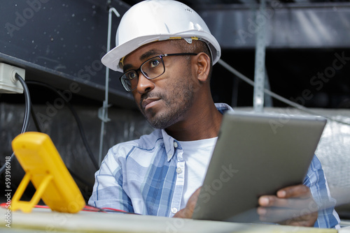 electrician working in roofspace using multimeter and tablet photo