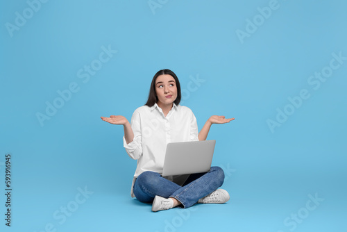 Puzzled young woman with laptop on light blue background © New Africa