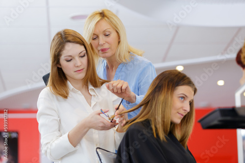 trainee hairdresser trimming customers hair under supervision