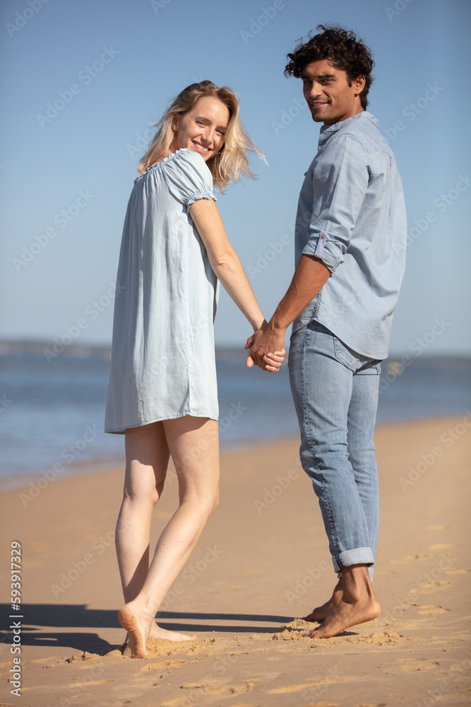 young couple walks hands along the sea coast back view young couple walks hands along the sea coast back view