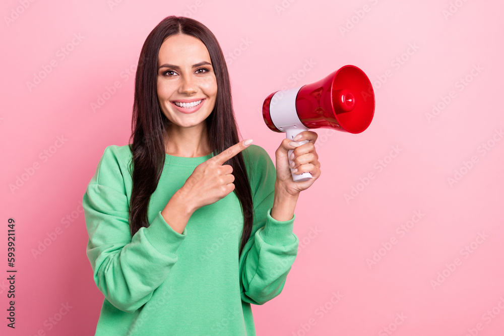 Portrait of cheerful positive girl straight hairstyle wear green pullover directing at loudspeaker isolated on pink color background Portrait of cheerful positive girl straight hairstyle wear green pullover directing at loudspeaker isolated on pink color background