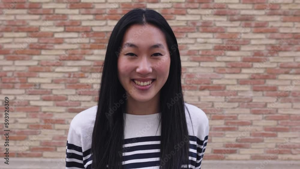 Happy young asian woman smiling at camera standing over brick background wall. Chinese people concept Happy young asian woman smiling at camera standing over brick background wall. Chinese people concept