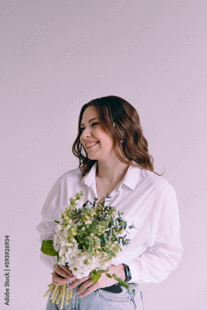 Luxurious girl with beautiful makeup and hairstyle, permanent makeup specialist, holds tools in her hands. Photoshoot in a photo studio in a suit, jeans and a shirt.