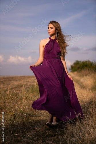 Vertical shot of a Caucasian blonde woman wearing a purple dress posing in a wild nature