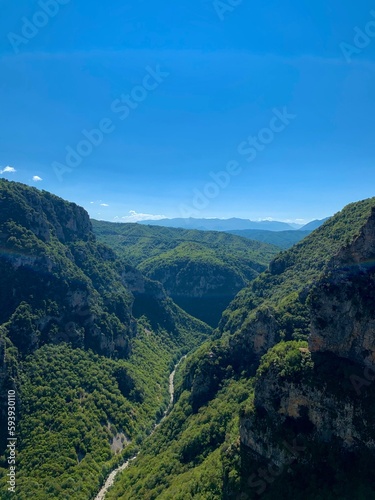 Vikos gorge, panoramic view of forestеd slopes, massive limestone cliffs, Voidomatis riverbed bends, and distant Pindus mountain randes from Beloi Viewpoint. Vikos-Aoos National Park, Zagori, Greece.