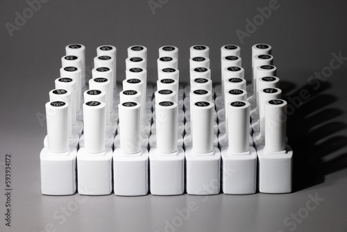 White bottles of gel nail polish with a palette of samples on a gray background. Layout for manicure or pedicure, template with copy space. Lots of vials displayed in rows.