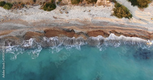 Flying drone over the coastline of the island overlooking rocky shoreline with vegetation and rocks and clear sea with light foamy waves in Cyprus.