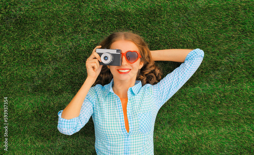 Summer portrait of happy smiling young woman photographer taking pictures on camera lying on the grass in the park