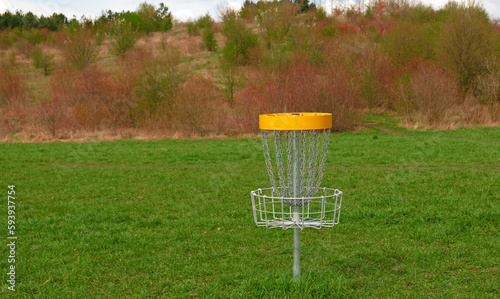 Disc Golf basket. Frisbee golf is sport and hobbie in outdoor park. Metal basket with chains for disc game surrounded by vibrant green trees.