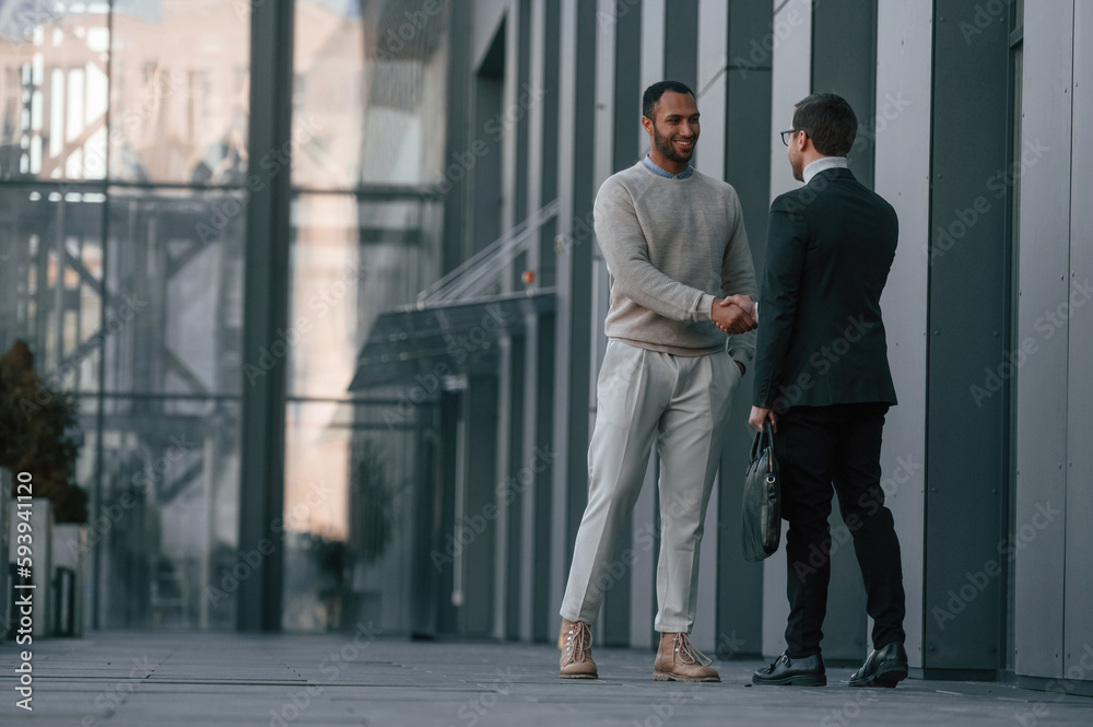Doing handshake, greetings gesture. Businessman in formal clothes is with black man outdoors in the city Doing handshake, greetings gesture. Businessman in formal clothes is with black man outdoors in the city