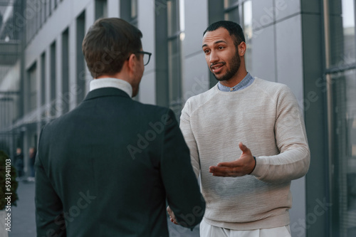 Businessman in formal clothes is with black man outdoors in the city