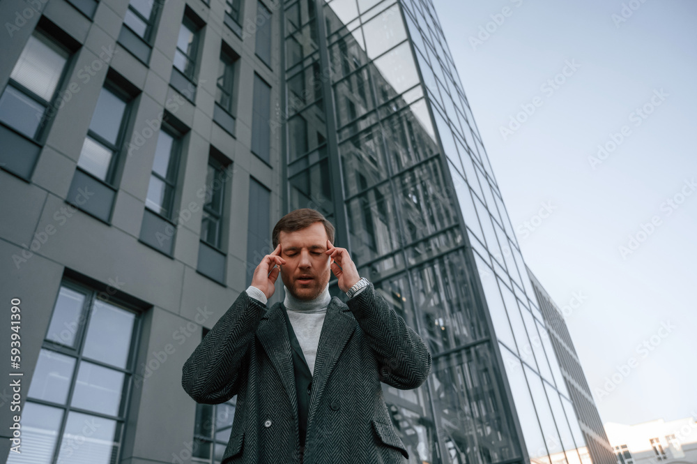 Having headache, feeling bad, stressful. Handsome man in formal clothes is outdoor near the business building Having headache, feeling bad, stressful. Handsome man in formal clothes is outdoor near the business building
