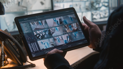 Male security officer controls CCTV cameras in office, uses digital tablet and computers with surveillance camera footage playback on screens. High tech security system. Monitoring and social safety.