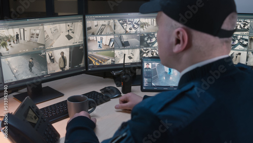 Security officer controls CCTV cameras with facial recognition in office, uses digital tablet and computers. High tech software with surveillance cameras playback on screens. Concept of social safety.