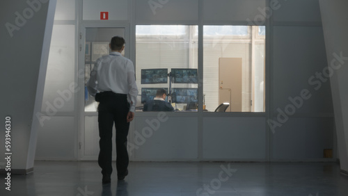Security officer in uniform comes in observation room, sits at the table with male coworker and controls CCTV cameras displayed on computer monitors. High tech security. Concept of social safety.